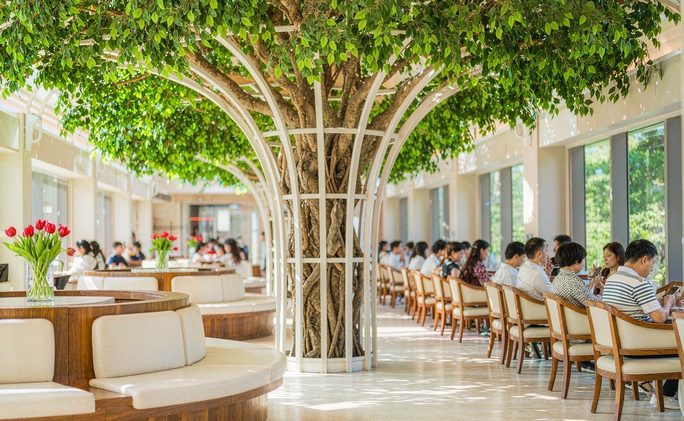Sculptural arched artificial ficus canopy sheltering a café seating deck in a transit concourse