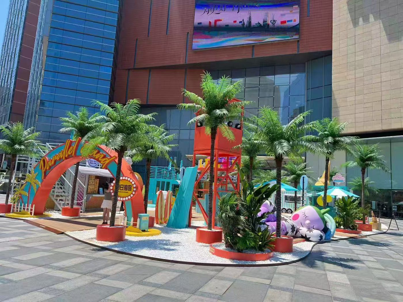 Artificial palm trees in red planters decorating a summer theme zone outside a shopping mall
