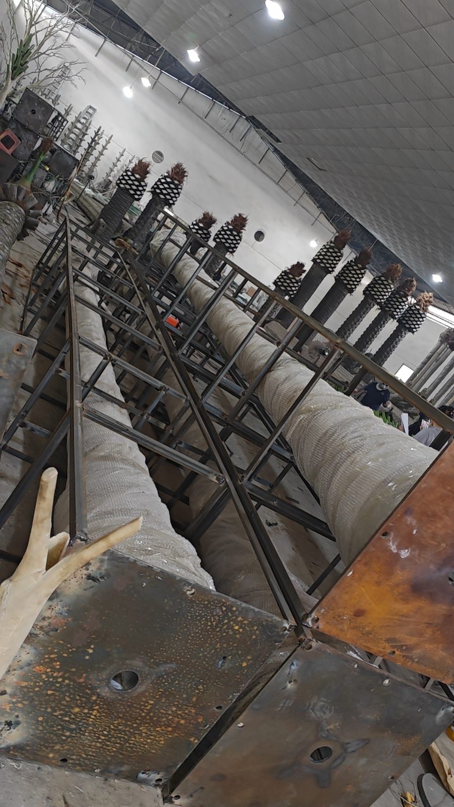 Welded steel frame surrounding a palm tree trunk inside the manufacturing workshop