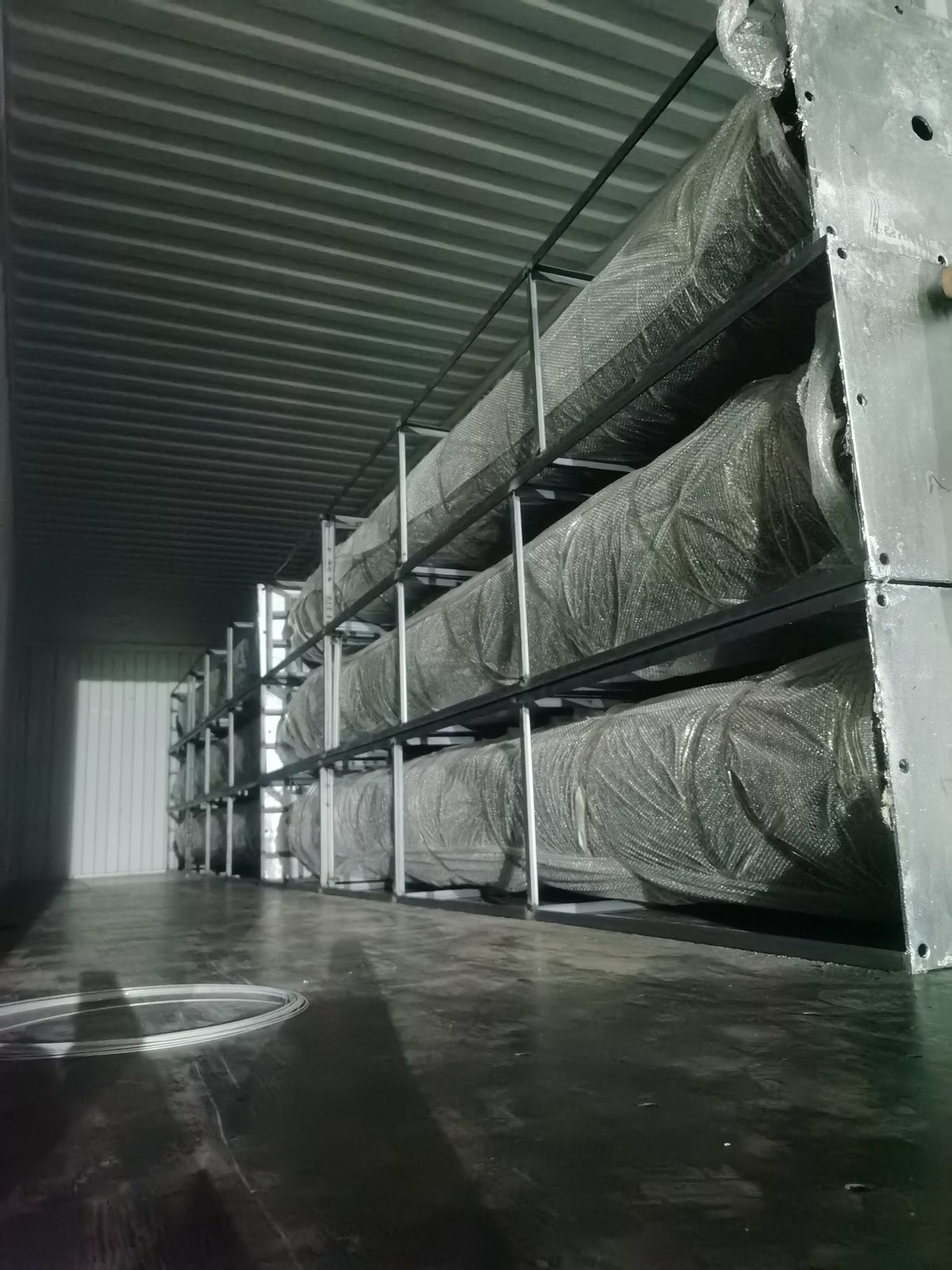 Export container interior loaded with wrapped artificial tree sections on tiered steel shelving