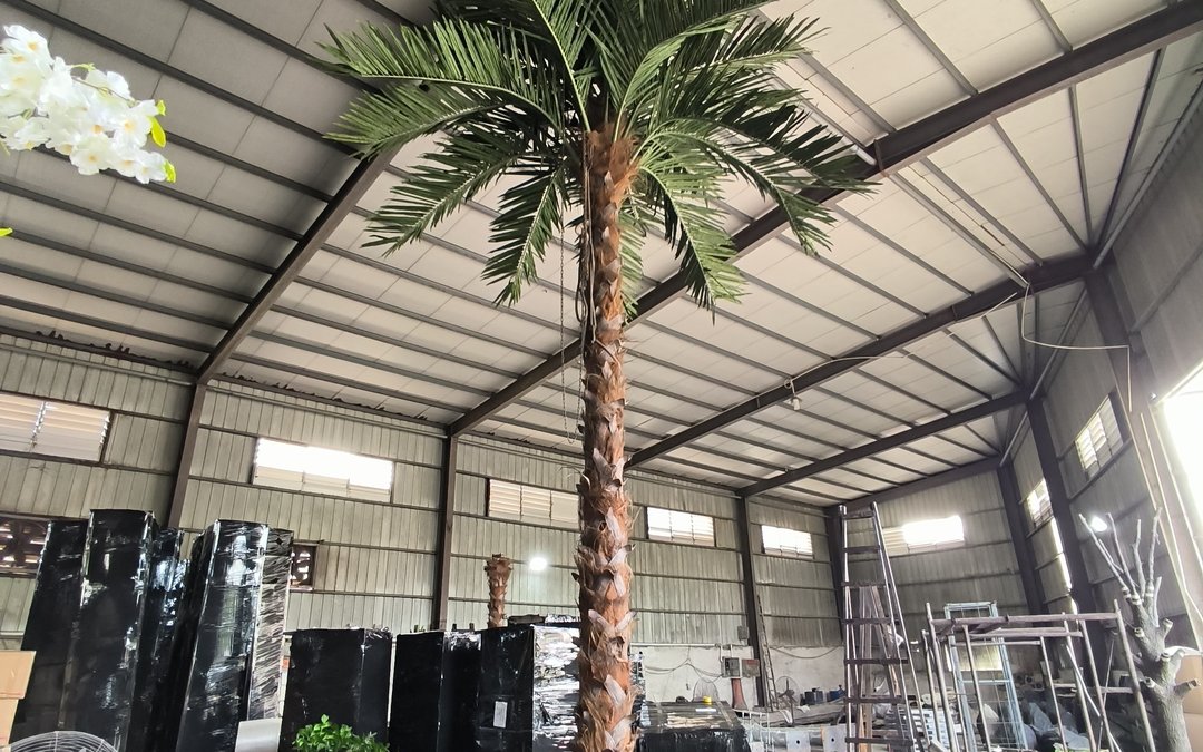 Tall artificial palm standing in the factory bay with a moulded trunk and green fronds