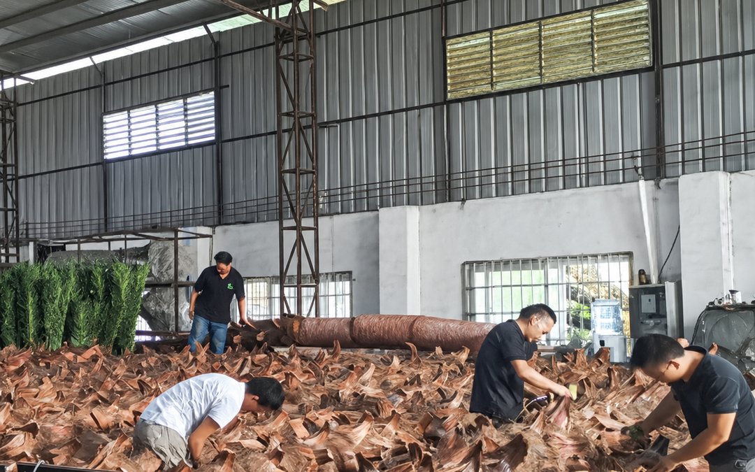 Bulk moulded leaves spread across the workshop floor being sorted by workers, with rolled trunk pieces beside them