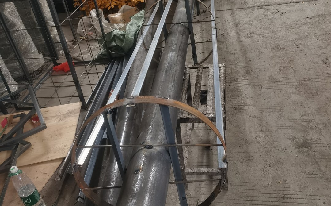 Galvanized square-tube frame and a bent steel hoop on a workshop floor beside a large core pipe