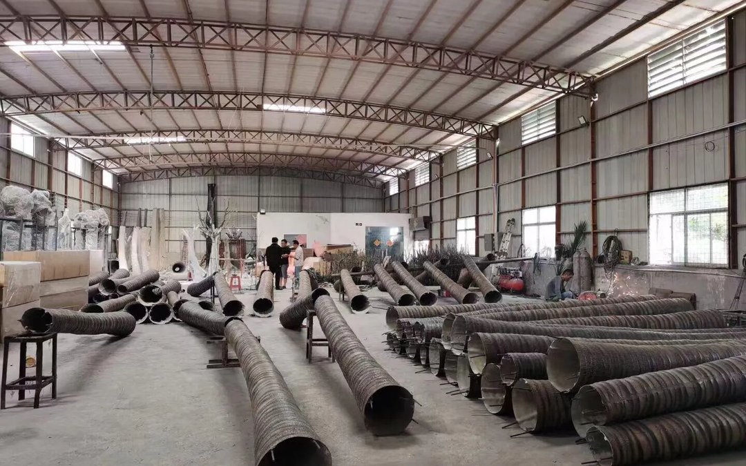 Long moulded trunk stock staged on the floor of a production hall beside wrapped foliage