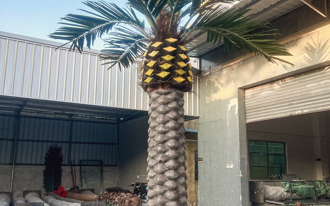 Artificial palm standing in the works yard with a banded crown base against a blue sky