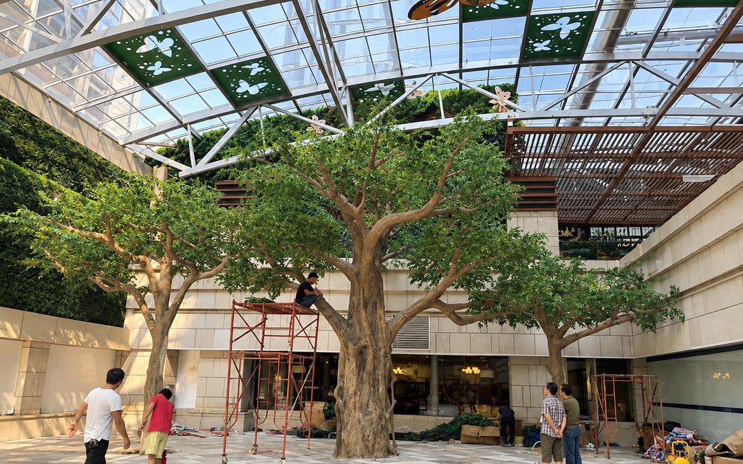 Large artificial ficus build being dressed in a glass-roofed commercial atrium