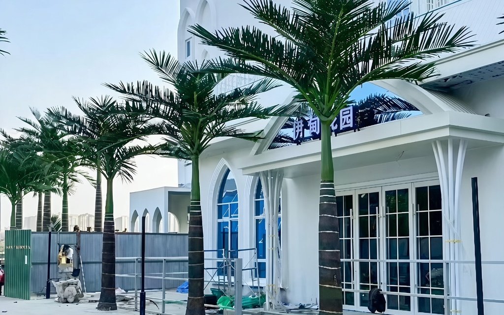 A row of artificial palms in front of a white building under fit-out, hoarding still standing