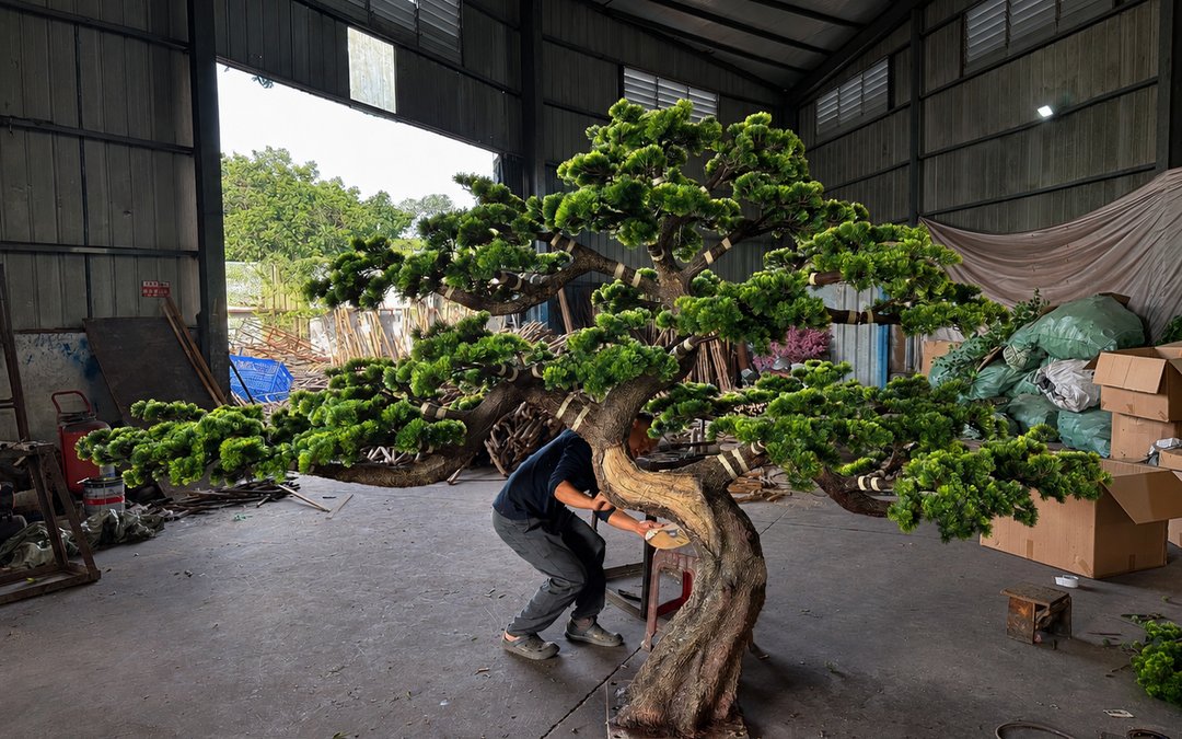 A large artificial pine tree being assembled in the workshop with a worker at the base