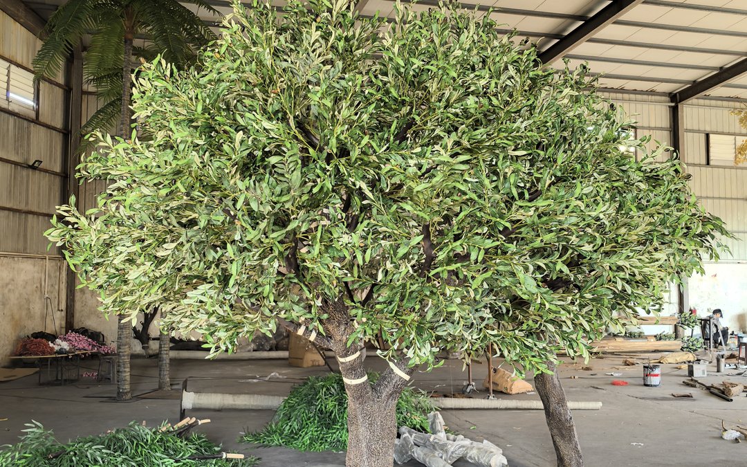 Large artificial olive-style tree standing in the workshop with a banded trunk and green foliage offcuts on the floor