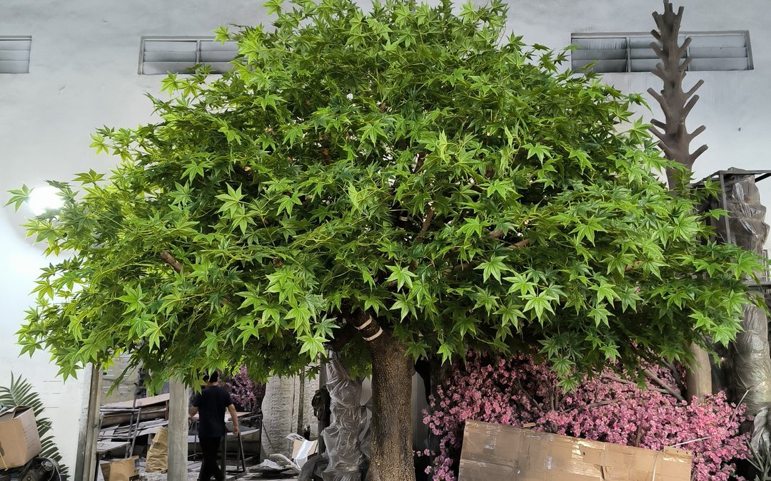 Green canopy tree assembled in the workshop with its trunk base visible, a bare steel armature and packing materials behind