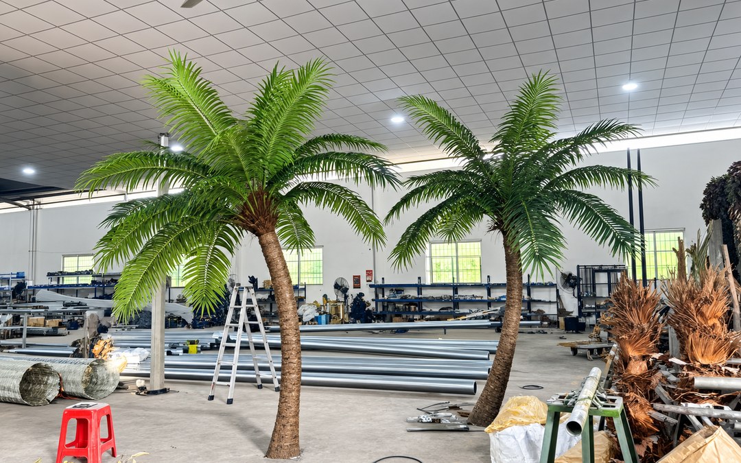 Two assembled date palms inside a factory workshop with galvanized tube stock on the floor