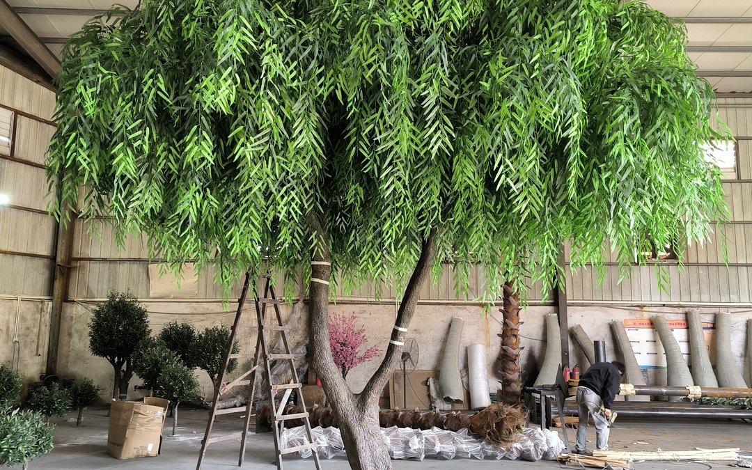 A large artificial tree with wrapped trunk lengths and staged components inside a production workshop