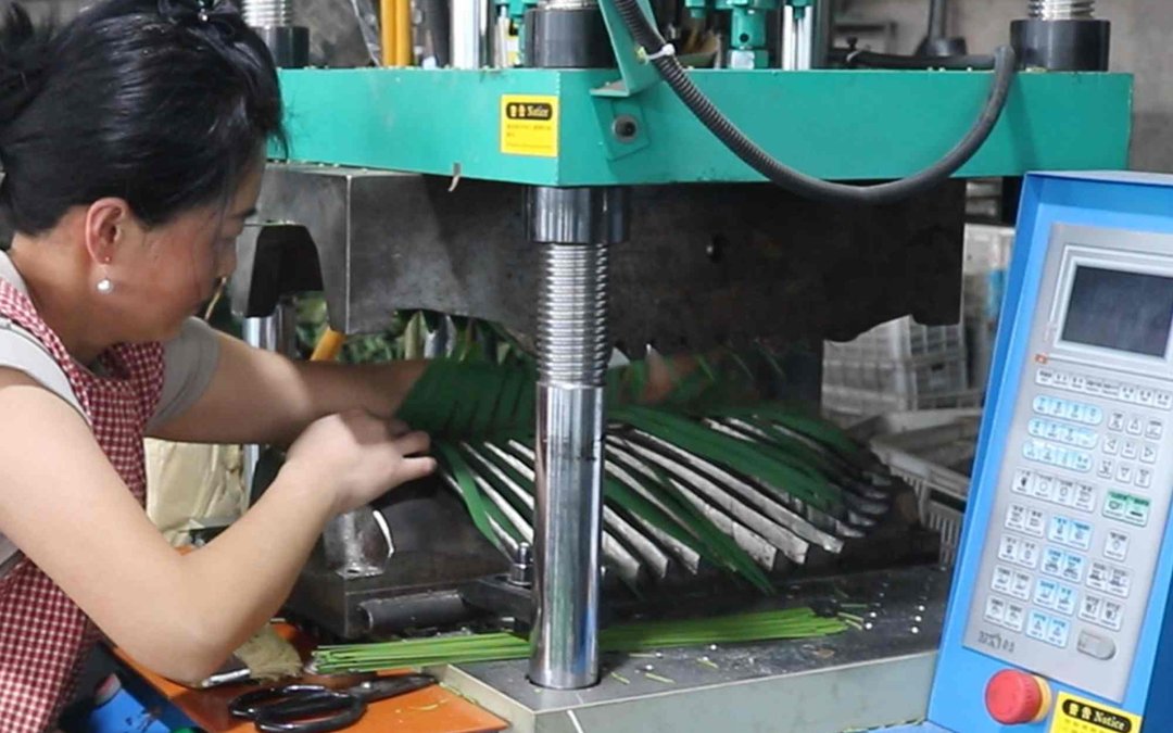A worker assembling palm frond strips at the pressing station in the production hall