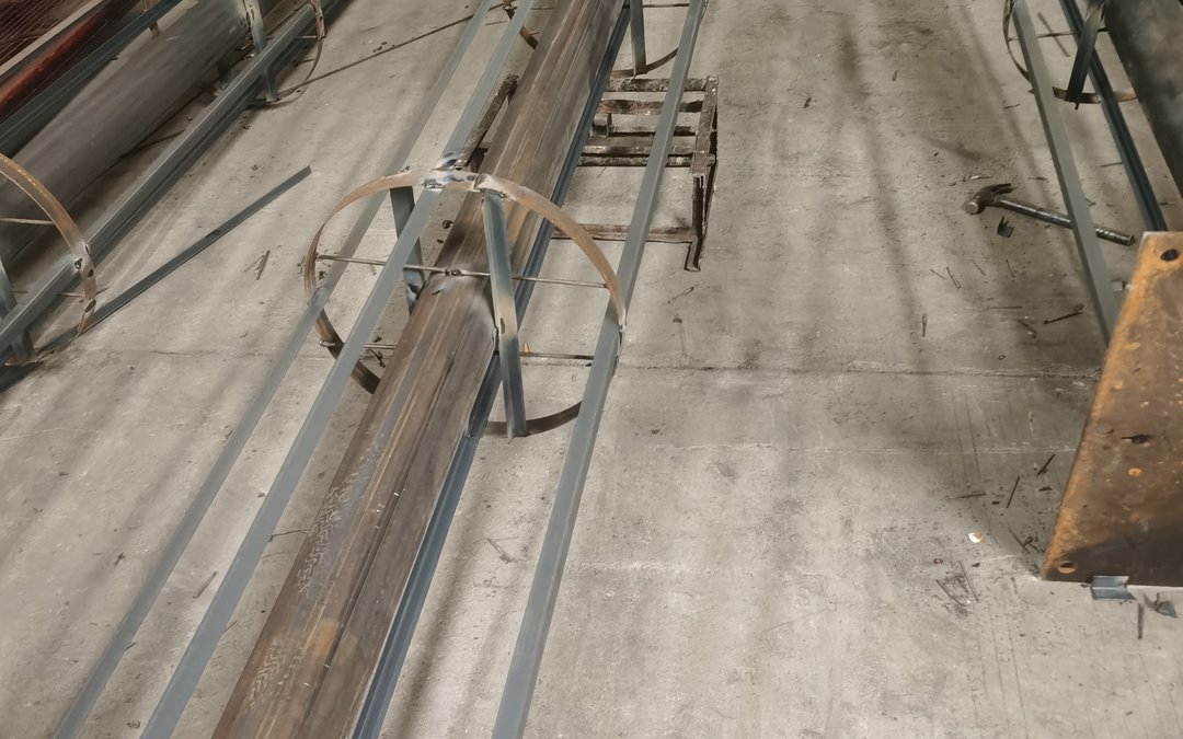 A knocked-down steel trunk core on the workshop floor with its welded branch brackets and a drilled base plate alongside