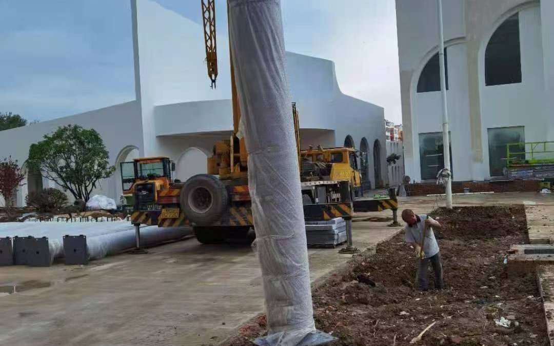 Film-wrapped artificial palm trunk standing beside a mobile crane on an outdoor installation site