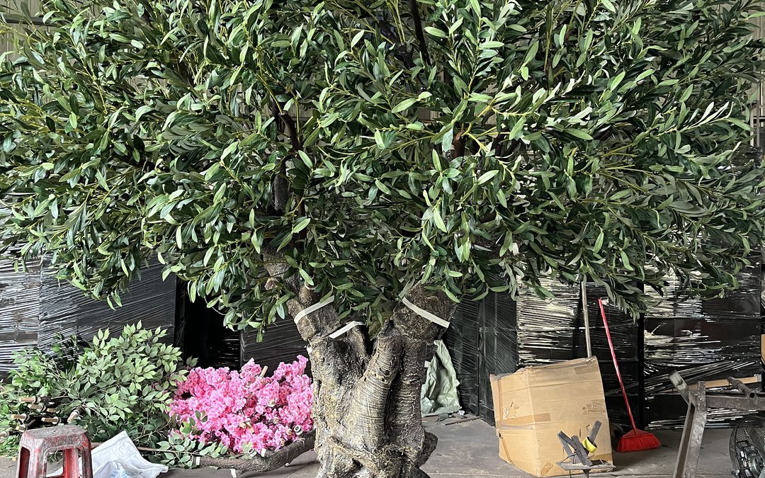 Large artificial olive tree in the workshop surrounded by film-wrapped stock and cartons