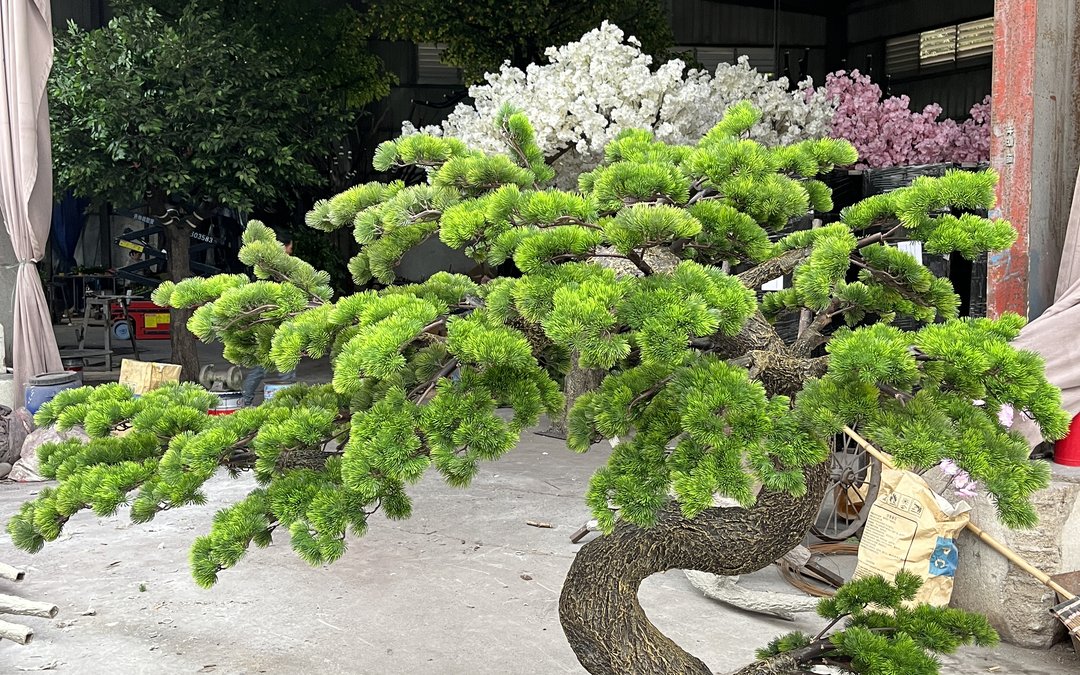 Bonsai-style artificial pine tree in the factory yard among blossom trees