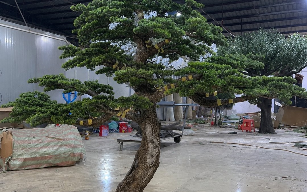 A large artificial banyan standing in a production hall, crown spread visible against the structural bays