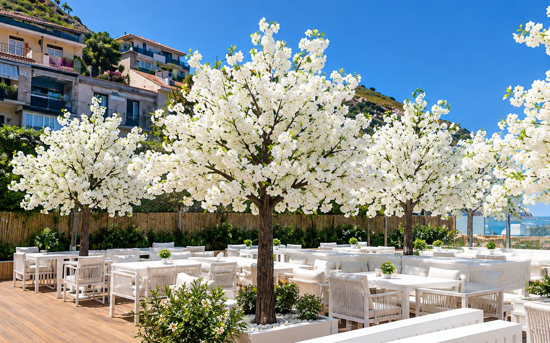 White blossom artificial trees on a seaside restaurant terrace with white dining furniture