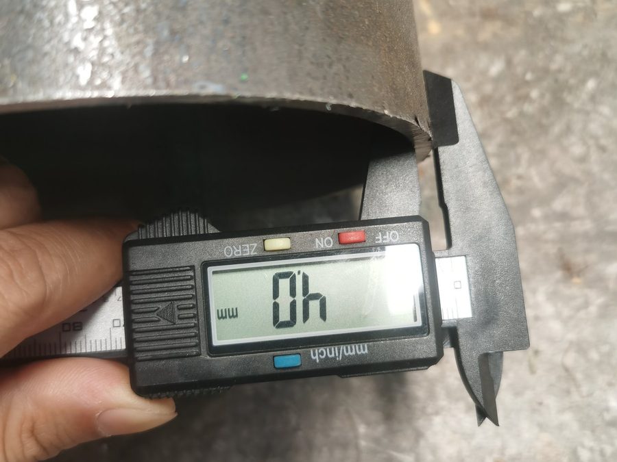 Digital caliper measuring the wall thickness of a steel trunk section
