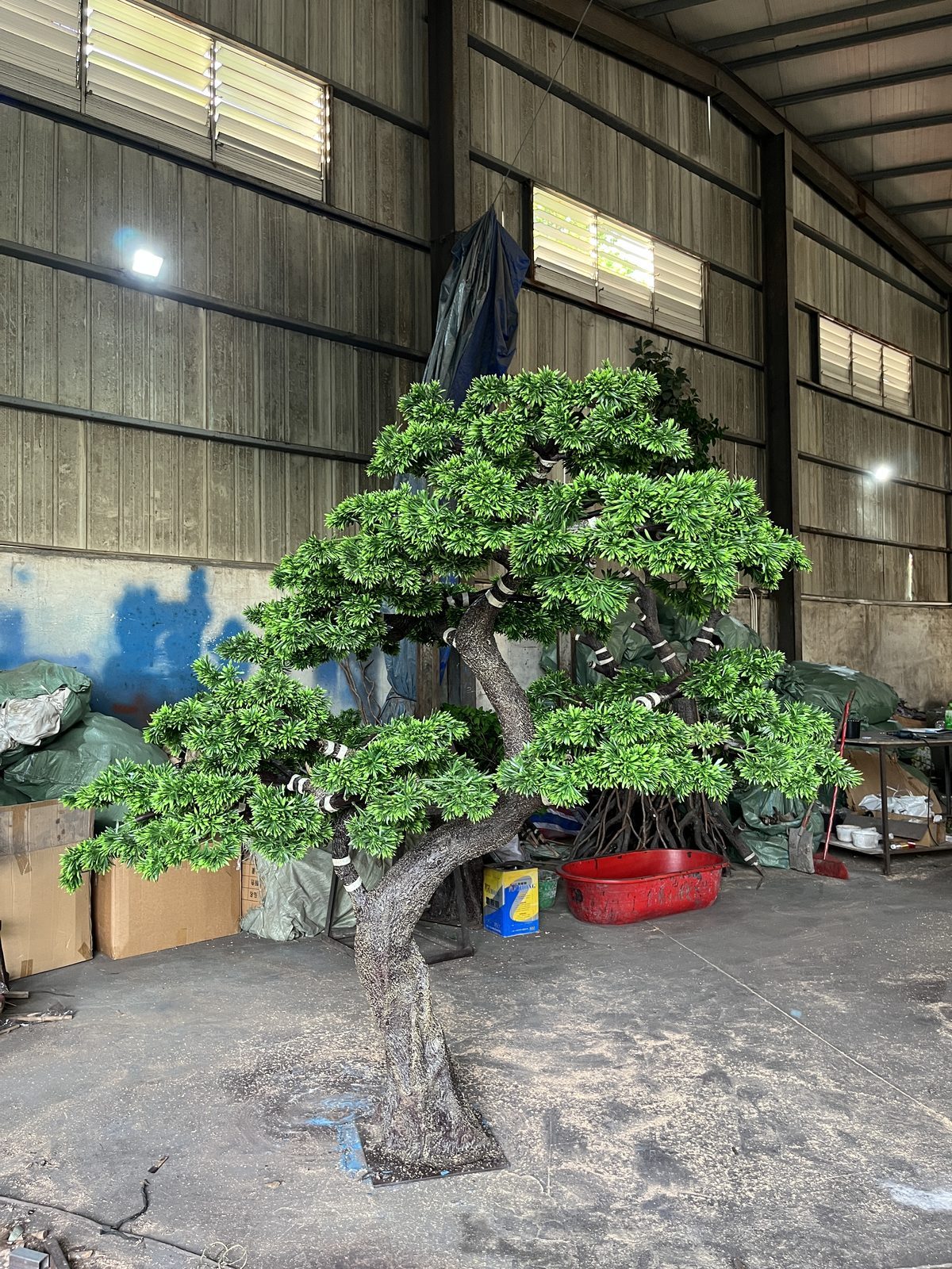 Artificial topiary pine with long horizontal branch tiers standing in our factory