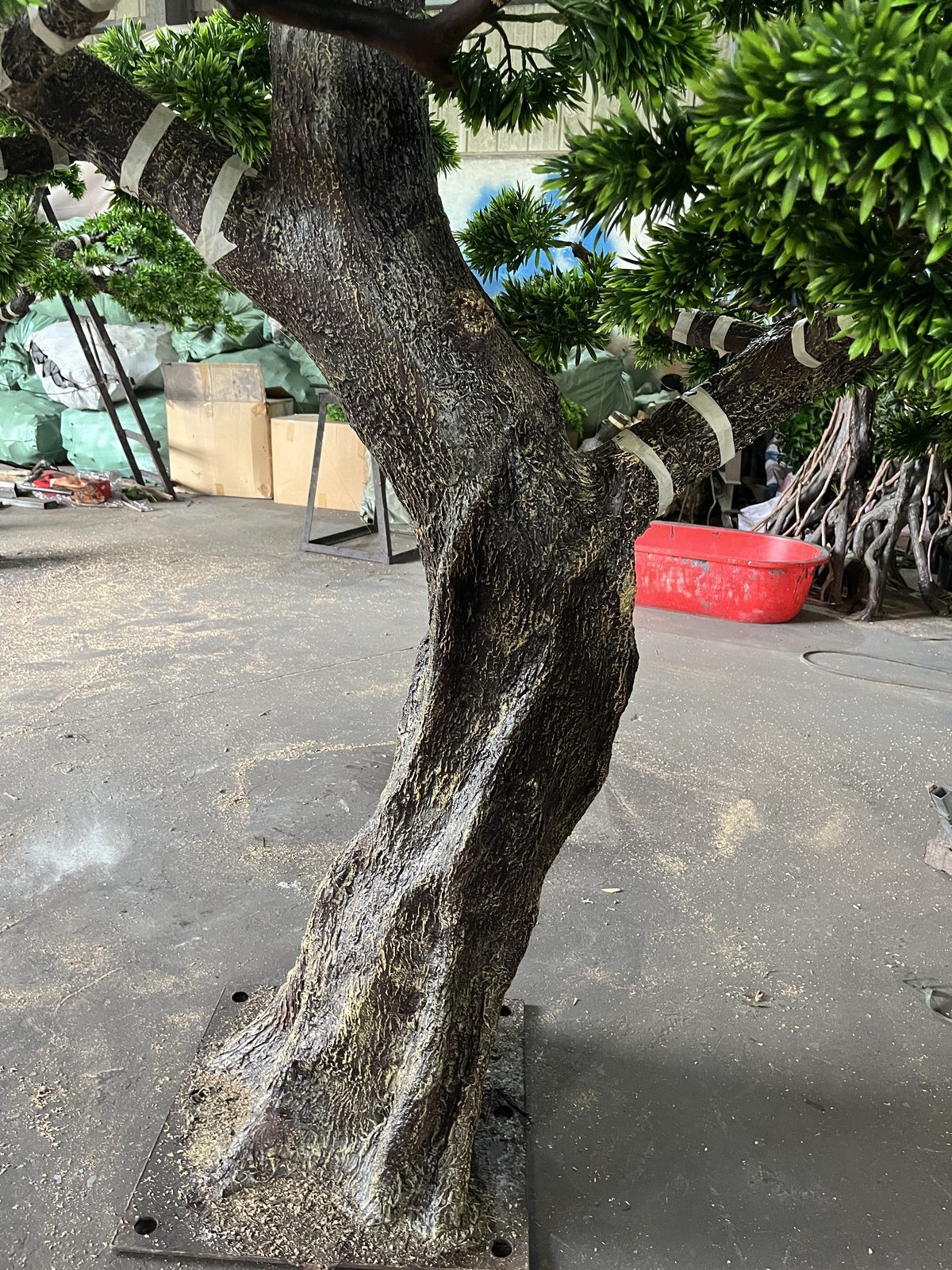 Close view of the sculpted bent trunk of an artificial topiary pine on its base plate